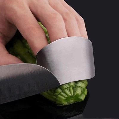 A person protecting his fingers with a steel finger protector when cutting zucchini