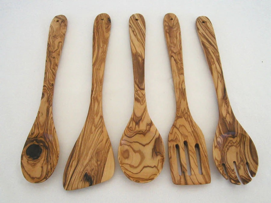 Close-up of a hand-carved olive wood spoon from the kitchen utensil set, highlighting the smooth finish and unique wood grain patterns.