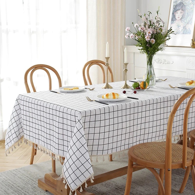 A table set for four with a casual cotton tablecloth, featuring a unique touch with tassels on the sides for added charm.